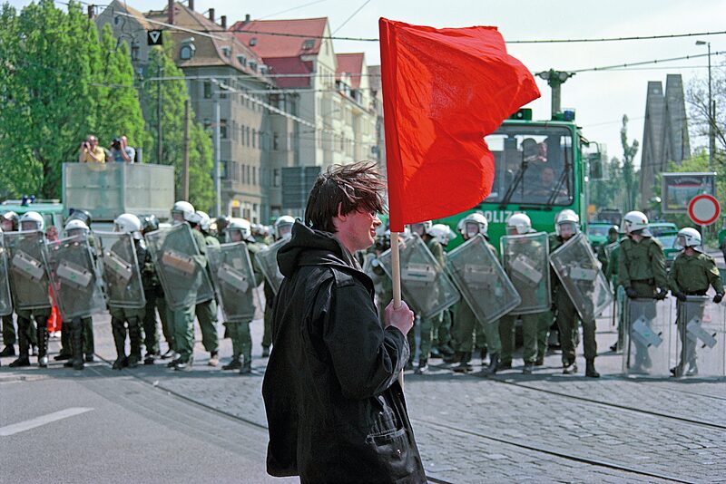Junger Mann mit roter Flagge vor Polizeikette