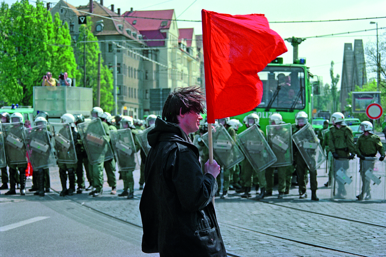 Junger Mann mit roter Flagge vor Polizeikette